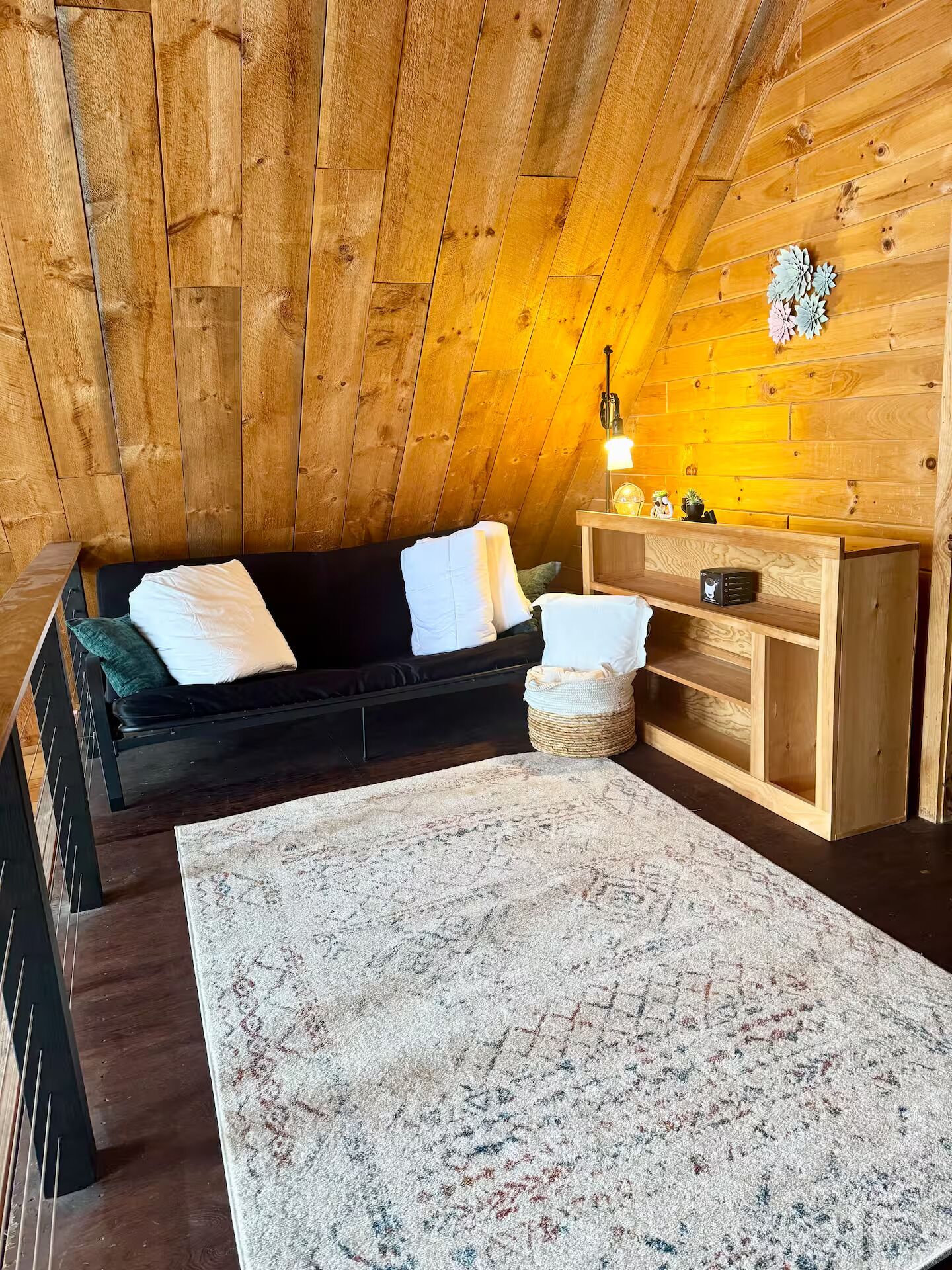 Une pièce chaleureuse avec un canapé sombre, un banc en bois, un panier tressé et une petite table avec une lampe.