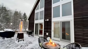 A covered outdoor deck with a fire pit and a heater, surrounded by snow-covered trees. - Cozy Chalet – Mtn View+ Hot Tub+ Hike+ Santa's Vil (Lancaster)