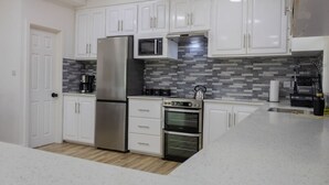 A modern kitchen with white cabinets, a stainless steel refrigerator, a microwave, a gas stove, and an oven. - Sea and Summit Suite #1 (Castle Comfort)