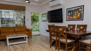 A living room with a brown sofa, wooden dining table, and chairs, a coffee table, and a TV on the wall. - Sea and Summit Suite #1 (Castle Comfort)