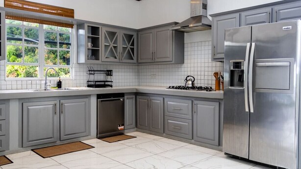 A modern kitchen with grey cabinets, a stainless steel refrigerator, and a window with a view of greenery. - Sea and Summit Villa (Roseau)