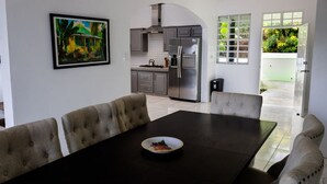 A modern kitchen with grey cabinets, a stainless steel refrigerator, and a dining area with a dark table and beige upholstered chairs. - Sea and Summit Villa (Roseau)