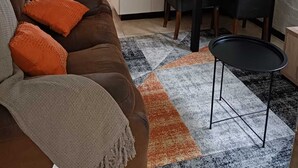 Un salón acogedor con un sofá de cuero marrón, cojines naranjas, una mesita redonda y un comedor con sillas.