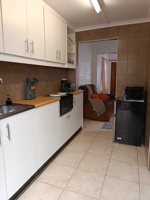 Una cocina compacta con armarios blancos, un refrigerador negro y una cafetera.