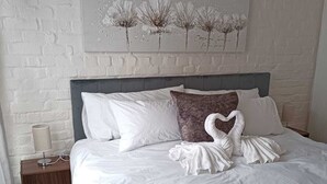 Una cama bien hecha con ropa de cama blanca y marrón, un cabecero y una obra de arte colgada en la pared.