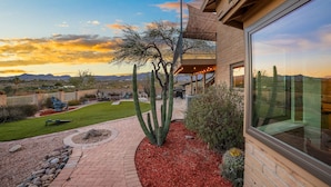 A modern house with a large glass window, a patio with a cactus garden, and a view of the desert landscape.