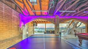 A ping pong table with a pool table in a covered area with brick walls and arched ceilings.