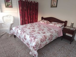 A bedroom with a bed, a nightstand, a chair, and a window with curtains.