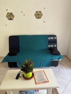 A teal sofa with black cushions, a small table with a remote control and a plant, and decorative hexagonal wall decals.