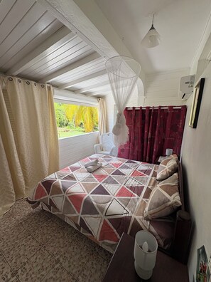 Ein Schlafzimmer mit Bett, einem Fenster mit Vorhängen, einem Nachttisch, einer Lampe und einem Deckenventilator.