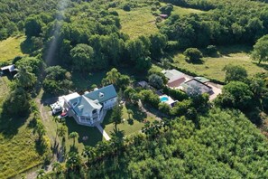 Vue aérienne d’une vaste propriété comprenant une maison principale, une piscine et une végétation luxuriante environnante.