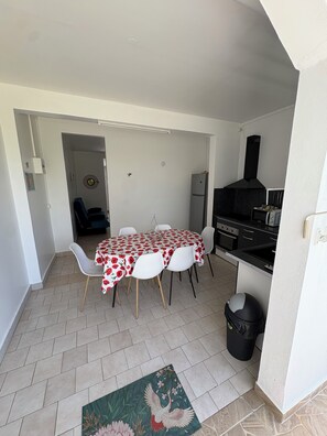 Ein Essbereich mit einem Tisch für vier Personen, eine Küche mit Herd und Kühlschrank sowie ein Mülleimer.