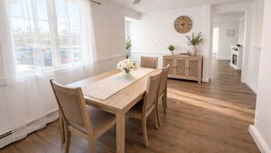 En matplats med ett träbord, stolar, en takfläkt, en klocka och ett skåp med växter.