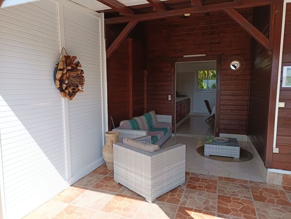 A covered patio area with a wicker sofa, a small table, and a decorative wall hanging.