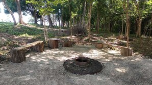 A circular fire pit surrounded by wooden benches and a gravel area in a forested setting.