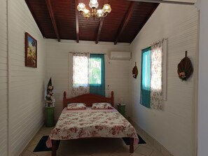A bedroom with a wooden bed, floral bedding, a chandelier, and two windows with curtains.
