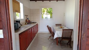 Una cocina compacta con comedor, que presenta suelo de baldosas, muebles de madera y un ventanal con vistas a zonas verdes.