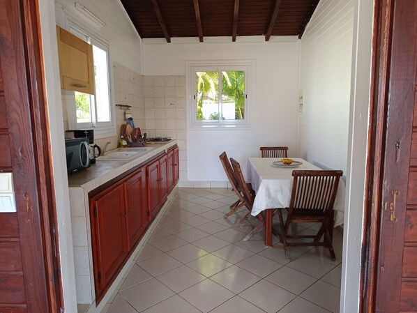 Una cocina compacta con comedor, que presenta suelo de baldosas, muebles de madera y un ventanal con vistas a zonas verdes.