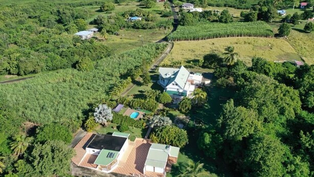 An aerial view of a property with a large house, a swimming pool, and surrounding lush greenery.