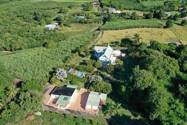 Vista aérea de una propiedad con una casa grande, una piscina y exuberante vegetación circundante.