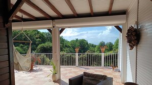 A covered patio with a wicker sofa, a hammock, and potted plants.