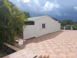 Un edificio blanco con techo verde, rodeado de palmeras y un patio empedrado.