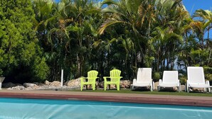 A swimming pool with clear blue water, surrounded by palm trees and lounge chairs.