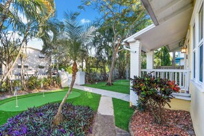 Welcome to a serene retreat surrounded by lush gardens and mature trees, with a paved pathway leading to a charming porch.