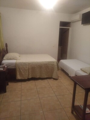 A small, dimly lit room with two beds, a wooden nightstand, and a small table.
