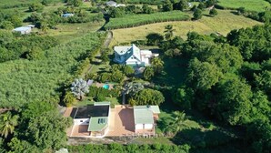 An aerial view of a property with a main house, a swimming pool, and surrounding lush greenery.