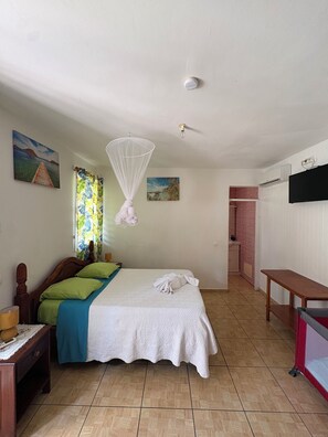 Una habitación de hotel con cama, mesita de noche, cortinas en la ventana, televisor montado en la pared y ventilador de techo.