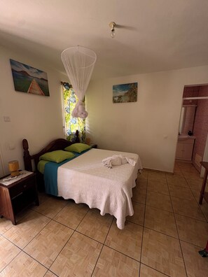 Una habitación con cama, mesita de noche, ventana con cortina y puerta que da a un baño.