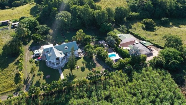 An aerial view of a property with a large house, a swimming pool, and a tennis court surrounded by lush greenery.