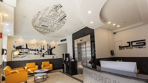 A hotel reception area with a modern design, featuring a reception desk, seating area with yellow chairs, and a wall with a New York City mural.
