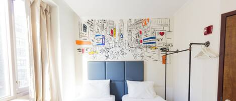 A hotel room with two beds, a large wall mural, a window with curtains, a radiator, and a wardrobe.