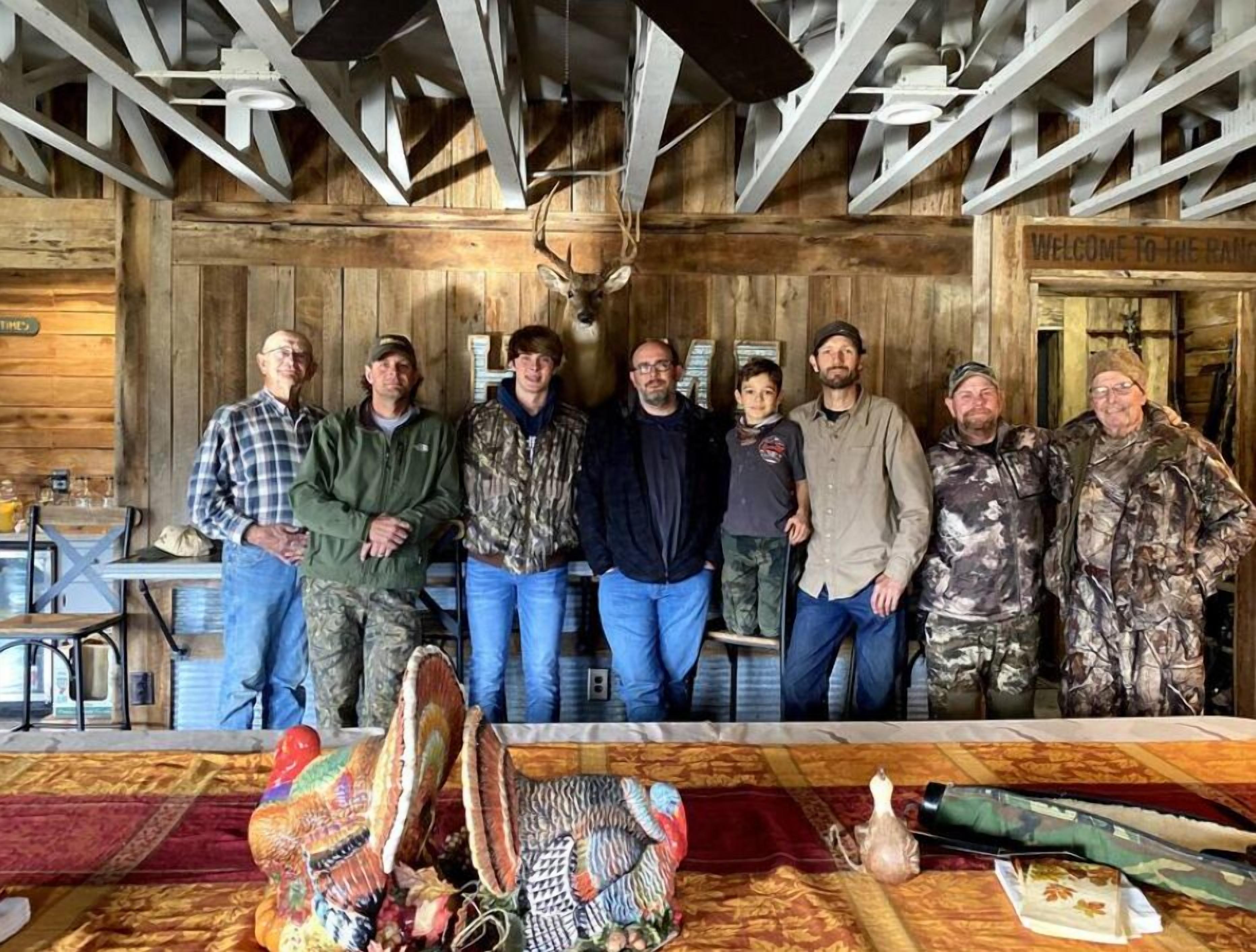 A group of people in a rustic room with wooden walls and a ceiling fan.
