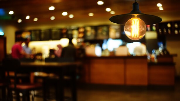 A bar with a hanging light bulb, wooden furniture, and a counter with people in the background. - Cozy hotel in Soho - 2 Double Beds (New York)