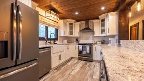 Una cocina moderna con refrigerador de acero inoxidable, gabinetes blancos, techo de madera y encimera de mármol.