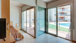 Een moderne hotelkamer met een bed, een bureau en een televisie. Er zijn grote schuifdeuren naar een balkon met een zwembad.