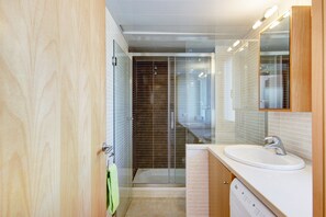 Enjoy a refreshing shower in the sleek bathroom with a glass-enclosed shower, white sink, and wooden cabinetry.