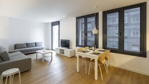 Uma sala de estar moderna com um sofá cinzento, uma pequena mesa branca e um espaço de jantar com uma mesa branca e cadeiras amarelas.