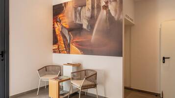 Un interior moderno con un cuadro abstracto grande, dos sillas de mimbre, una mesita de madera y una puerta con la inscripción 'ACCESSO GARAGI'.