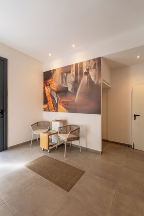A modern interior with a large abstract painting, two wicker chairs, a small wooden table, and a door labeled 'ACCESSO GARAGI'. - Urbanfive 1A Ourense center 3 rooms with terrace (Ourense)