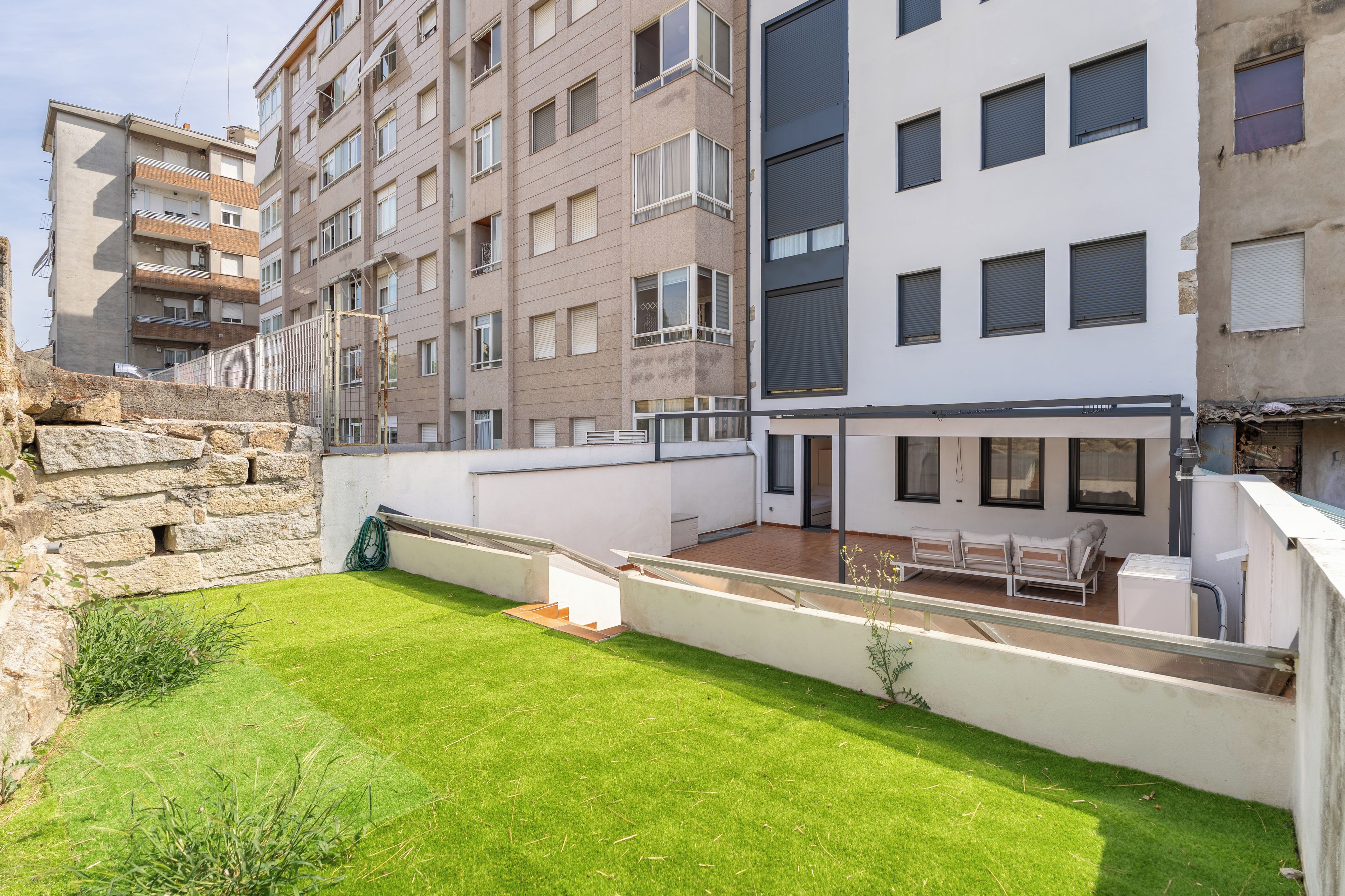A residential building with multiple balconies, a small courtyard with grass, and a white exterior.
