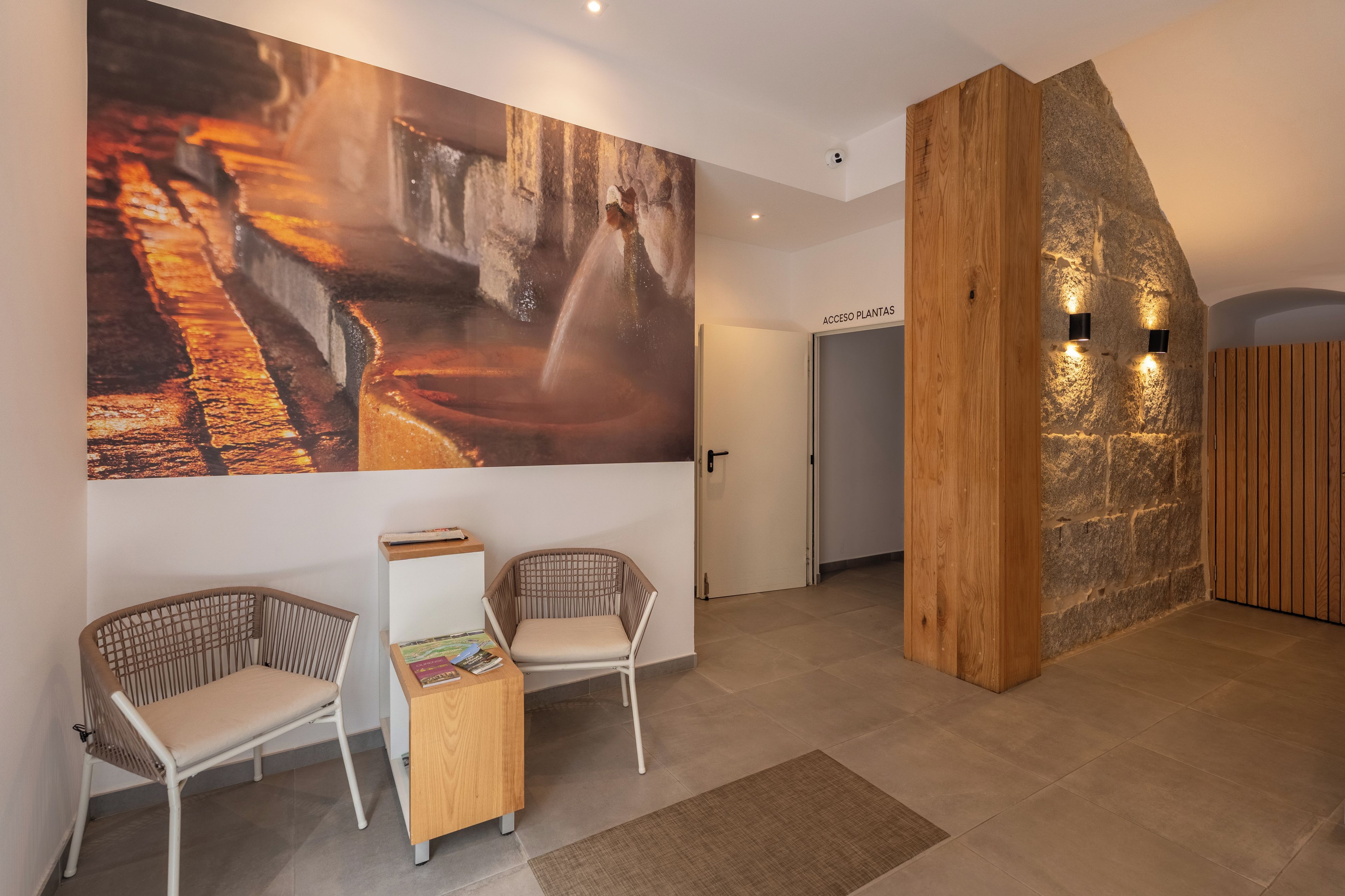 Ein modernes Interieur mit einem großen abstrakten Gemälde, zwei Korbstühlen, einem kleinen Holztisch und einer Rezeption mit einer Wand aus Stein und einer Holzwand.