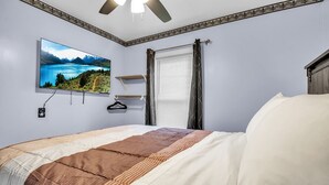 Un dormitorio con cama, televisor montado, ventana con cortinas y ventilador de techo.