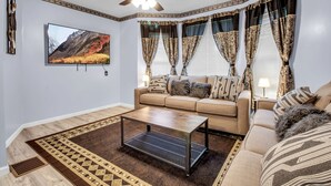 Un salón con un sofá color beige, una mesa de centro y un televisor montado en la pared.
