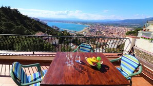 Una mesa de madera con sillas en un balcón con vistas a una ciudad costera.