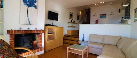 Uma sala de estar com lareira, um sofá, uma televisão e escadas que levam a um andar superior.