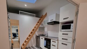 A compact kitchen with white cabinets, a built-in microwave, and a wooden ladder leading to a lofted storage area.